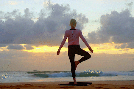 Woman holding a yoga tree pose on a beach at sunrise