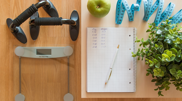 Scale, dumbbells, measuring tape, and food journal arranged for summer weight loss planning
