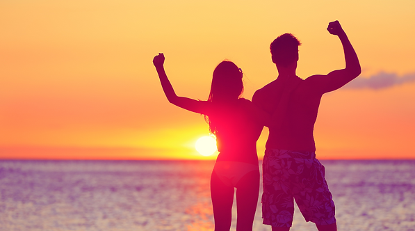 Couple celebrating with raised arms at sunset after reaching fitness goals